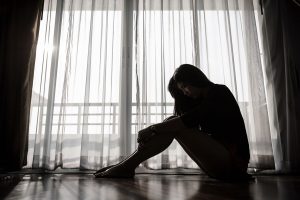 Symbolbild Depression: Frau sitzt im abgedunkelten Zimmer auf dem Boden
