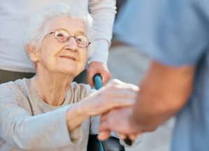 Holding hands, caregiver and senior woman in wheelchair for support outdoor in retirement home. Love, trust and healthcare nurse or medical wellness doctor for disability patient with kindness