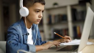 Junge mit aufgesetztem Kopfhörer bei der Arbeit an einem Laptop