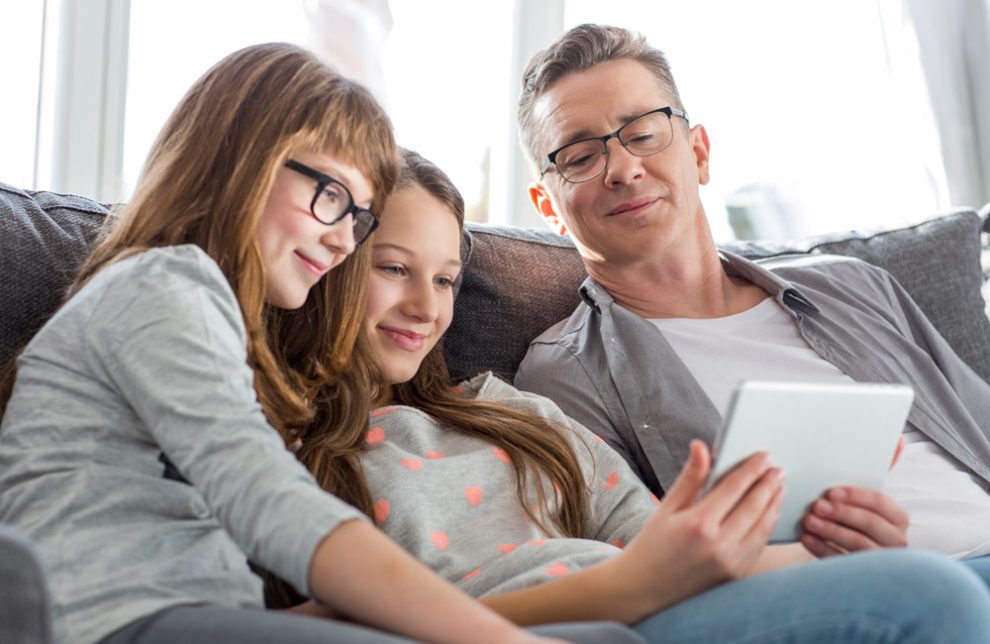 Symbolbild Familie: Zwei Mädchen und ein Mann auf einem Sofa