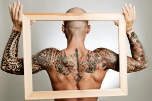 Rückenansicht eines Mannes mit Tattoos auf Rücken, Schultern und Armen