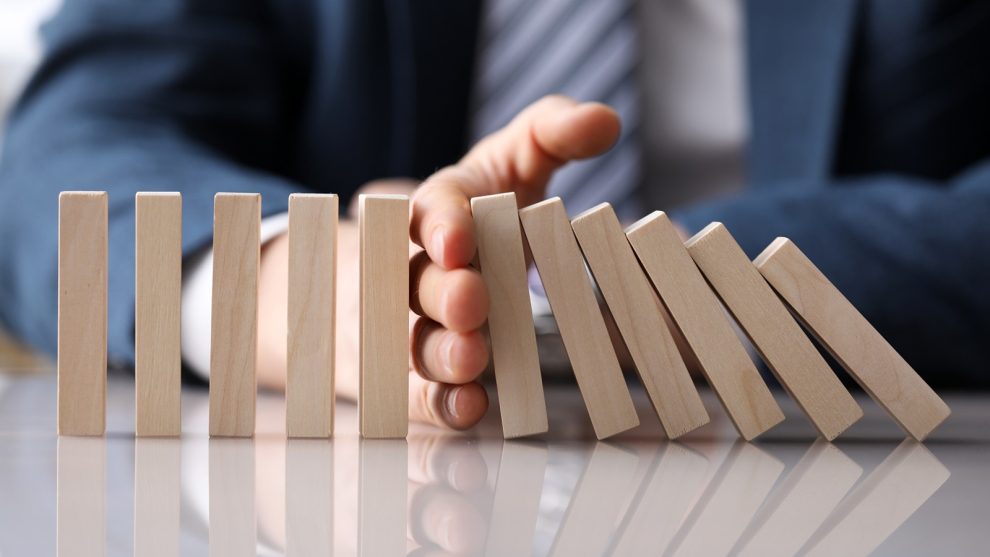 Business man in suit holding with hand falling sequence of wooden blocks closeup