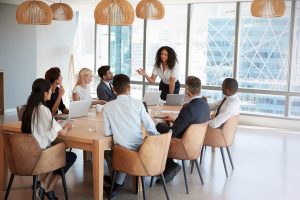 Businesswoman Stands To Address Meeting Around Board Table